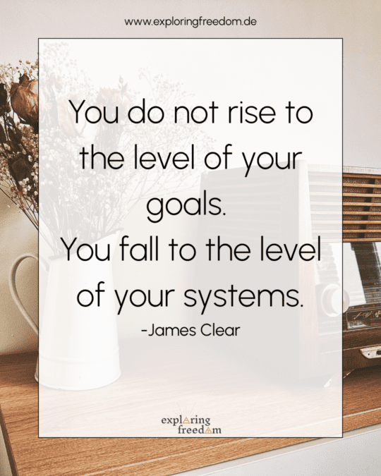 Zitat von James Clear: 'You do not rise to the level of your goals. You fall to the level of your systems.' auf hellem Hintergrund mit Vase und Radio