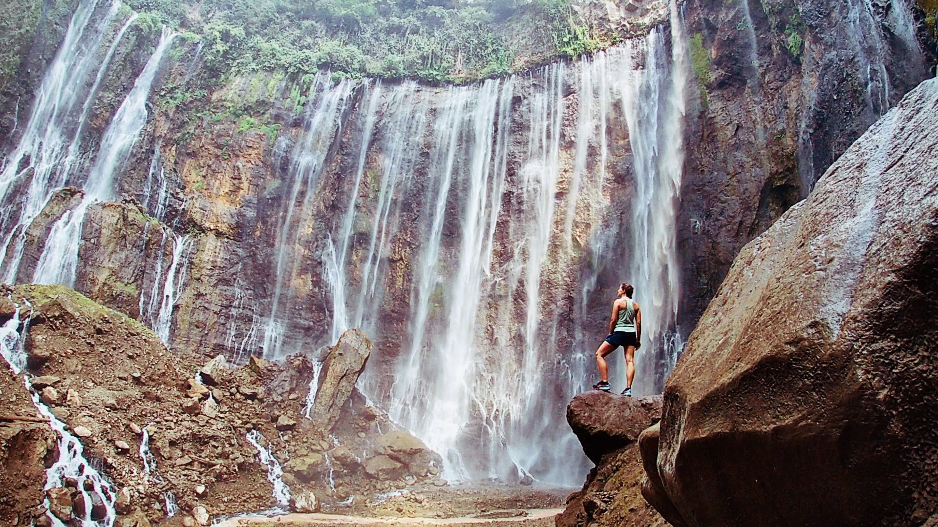 Frau steht auf Felsen vor einem breiten Wasserfall in einer felsigen Schlucht. Das Bild steht symbolisch dafür, wie man Veränderung im Leben findet und dessen Herausforderung.