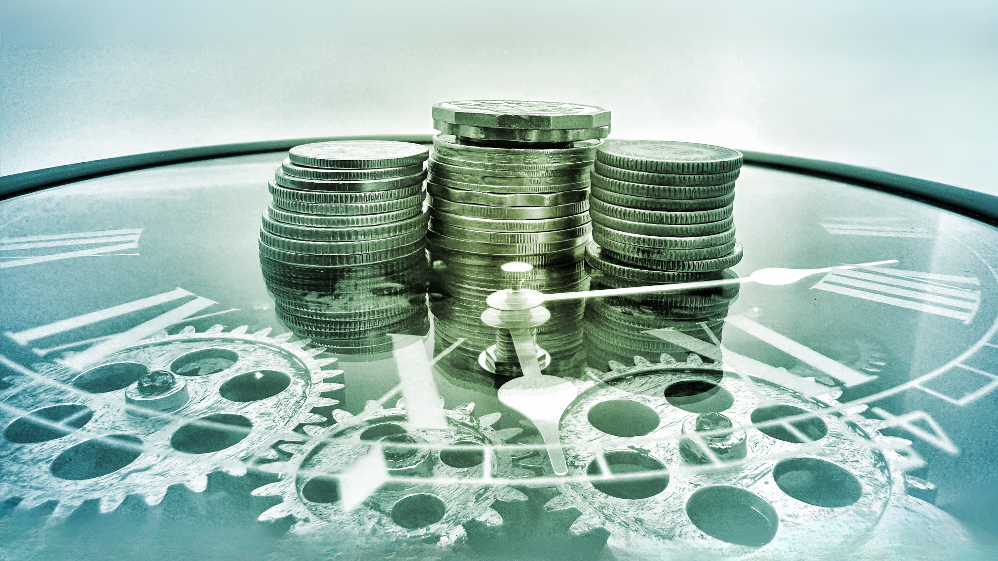 Mehrere Stapel Münzen auf einem Zifferblatt mit sichtbaren Zahnrädern. Steht symbolisch für Geldblockaden